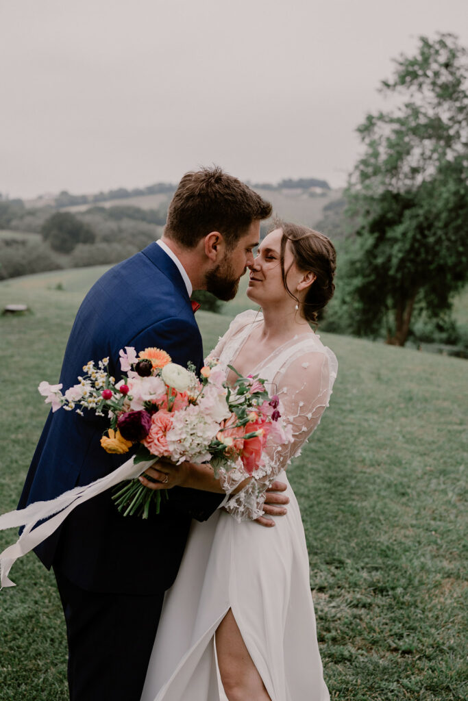 un couple d'amoureux s'enlace et se laisse porter par le vent qui emporte le ruban du bouquet de mariée déstructuré composé de fleurs champêtre et romantiques pour leur mariage au Domaine Etxezahar au Pays basque