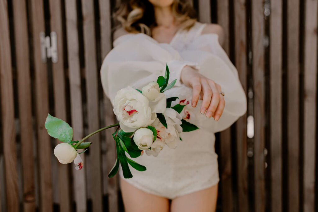 la modèle se tient les mains croisées en avant tenant des fleurs de pivoines blanches avec le cœur rose