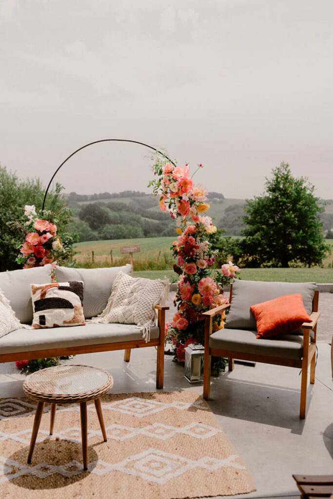 espace de la cérémonie laïque où vont s'assoir les mariés, avec en fond l'arche florale composée de fleurs dans les tons de orange rose et jaune dans un style floral champêtre et bucolique