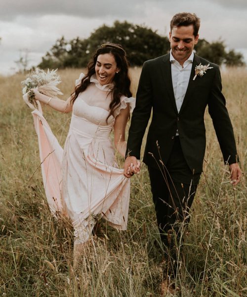 un couple de mariés ayant le sourire et se baladant main dans la main dans les champs autour du domaine de réception privé sur les hauteur de Ciboure au Pays basque